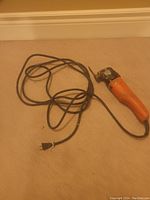 Full view of orange electric oscillating multi-tool with attached cord and plug