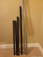 Photo showing six PVC pipe offcuts leaning against a wall: four black pipes and two white pipes with length markings. Pipes vary in length between 36 and 61 inches.