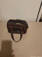 Front side view of the small vintage brown leather purse showing zippered compartments and handles.