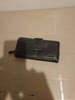 Closed view of black leather Roots wallet showing contrast white stitching and embossed logo.