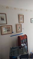 View of wall with five framed prints hung, showing arrangement and frame styles.
