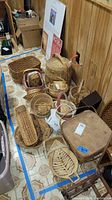Full overhead view of multiple baskets displaying variety of shapes and weave styles laid out on tile floor with wooden paneled wall background.