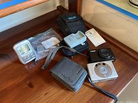 Overview photo of all items showing cameras, charger, battery, camera cases, clock and manuals on wooden surface.