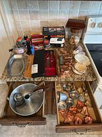 Overview of kitchen tools on countertop and in drawers showing knives, baking pans, cookie cutters, molds, sharpeners, and candles.