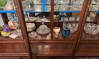 Wide view of the glassware and china pieces in a cabinet including cut glass bowls, covered dishes, art glass vase, and china bowls.