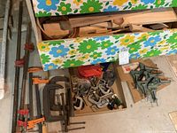 Multiple long pipe clamps with orange and black handles and assorted wooden boards seen in a floral drawer.