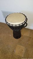 Front view of djembe drum showing natural skin drumhead, rope tuning, and wooden body with handle.