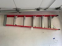 Full side view of the red fiberglass ladder with metal rungs hung on a wall.