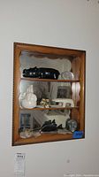 Front view of wooden wall shelf unit with mirror back, displaying various figurines: black carved fish, white elephant, small carved figures, and stone heads.