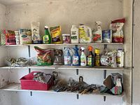 Full shelf view showing a wide assortment of garden chemicals in bottles and bags, hand tools, gloves in a plastic bin, and other materials