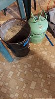 Overview of green Forane 22 cylinder next to black metal bucket on tiled floor