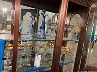 Overview of cabinet shelf showing decanter, gold-rimmed flutes, colored stemware