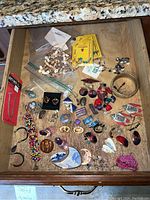 Drawer containing a wide assortment of handmade bracelets, earrings, pins, and decorative jewelry pieces, some broken or loose