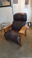 Right angled view of the brown leather recliner showing cushioned seat and back, and wooden arm sides with slatted panels.