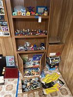 Wooden shelving unit with assorted toys figurines, children's books below, and Lego and model train items on the floor