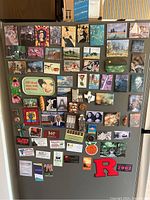 Full front view of refrigerator door showing all magnets, including art reproductions and multiple business card magnets.