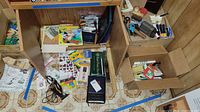 Top-down photo showing the variety of office supplies in boxes and loose on the floor, including scissors, markers, rulers, and other small office items.