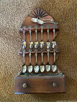 Front view of wooden rack holding 14 small spoons, rack has a drawer below.