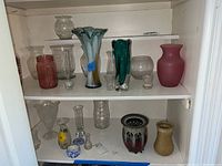 Shelf showing various vases and glass pieces including signed pottery vases and multiple glass art vases