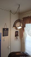 Vintage woven shade hanging light plugged in and hanging from ceiling chain in a room corner showing ambient lighting and adjacent wall decor.