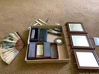 Overall view of vintage razors in cases, decorative fan, garter rose, and tri-fold mirror panels.