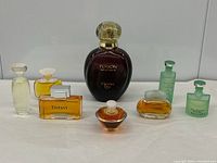 Front view of all seven perfume bottles arranged on white surface, large bottle centered with minis around.