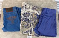 Three folded pairs of pants: blue denim jeans, beige paisley print trousers, cobalt blue dress pants
