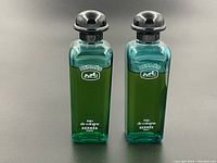 Front view of two green glass bottles with black caps on gray background