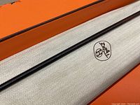 Close-up of riding crop resting on protective cloth inside orange box showing herringbone pattern and Hermes carriage logo
