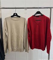 Two sweaters hung side by side on hangers: beige crewneck and red V-neck