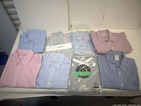 Eight folded men’s dress shirts laid out on table; various patterns and protective packaging visible