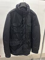 Front view of jacket hanging on rack showing overall style, pockets and closure.