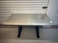 Straight on front view of table showing stainless steel top and black wood X-shaped base