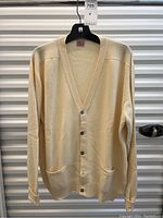 Front view of pale yellow cashmere cardigan on hanger showing V-neck, buttons and pockets