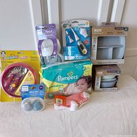 Full lot arranged with all included items: tableware set, diapers pack, thermometer kit, feeding bottle, soothers, and socks.