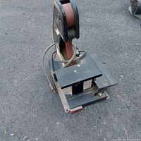 Front angled view showing the sanding belt, platform table, power cord coiled around the back, and the base with wear marks and dirt.