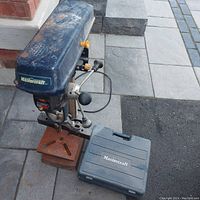 Full view of Mastercraft drill press with case for mortising kit on ground.