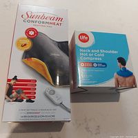 Boxed Sunbeam Conformheat heating pad and Life brand Neck and Shoulder Hot or Cold Compress, shown together on a surface.