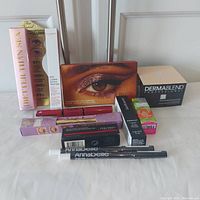 Lot of brand new makeup products including mascara, eyeshadow palette, loose powder, lip gloss, brow pencil, lip balm, lipstick, and eyeliners.