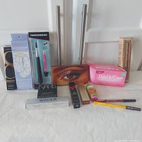 Full view of all makeup products displayed including mascara, eyeshadow palettes, reusable masks, lip glosses, eyeliners and a makeup eraser cloth.