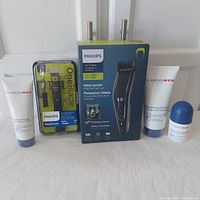 Full lot photo showing Philips OneBlade in plastic packaging, Philips Series 7000 hair clipper box, and Clarins Men skincare products.