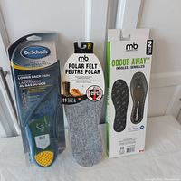 Photo showing all three types of insoles in packaging: Dr. Scholl's, M&B Polar Felt, and M&B Odour Away boxes.