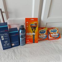 Gillette Fusion 5 razor handle with 2 cartridges, 12-pack and 8-pack Gillette replacement cartridges, Clarins Men shave gel and aftershave, Biotherm Homme foam all arranged in a row.
