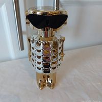 Gold-tone metallic bottle with decorative scale-like design, standing upright on a flat surface.