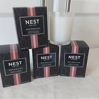 Four Nest New York Rose Noir & Oud scented candles in their original black boxes with pink vertical stripes and one candle out of the box showing the frosted glass container and white wax.