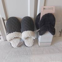 Photo showing the two pairs of new slippers side by side, one gray cable-knit with fluffy white lining, one black fuzzy flip flop style with packaging.