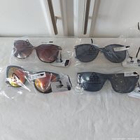 Four pairs of sunglasses in clear plastic PE-LD bags with tags, showing various frame and lens colors.