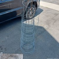 Stacked set of about 10 wire tomato cages shown outdoors next to a vehicle.