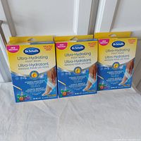 Three boxes of Dr. Scholl's Ultra-Hydrating Foot Mask with yellow and blue packaging, each box labeled as a value pack containing 3 pairs or 2 pairs of foot masks.