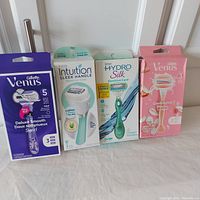 Photo showing four boxed women's razors from Gillette and Schick laid out on flat surface.